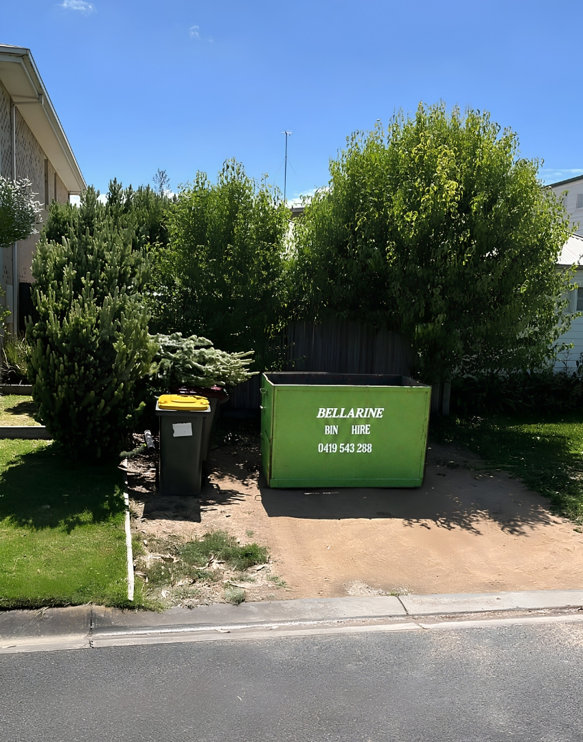 Green skip bin and yellow lid bin on a residential street with trees and buildings in the background.