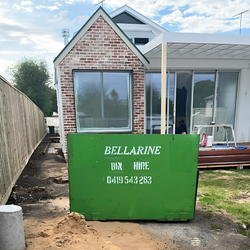 Green bin hire container with 'Bellarine Bin Hire' branding in front of a house.